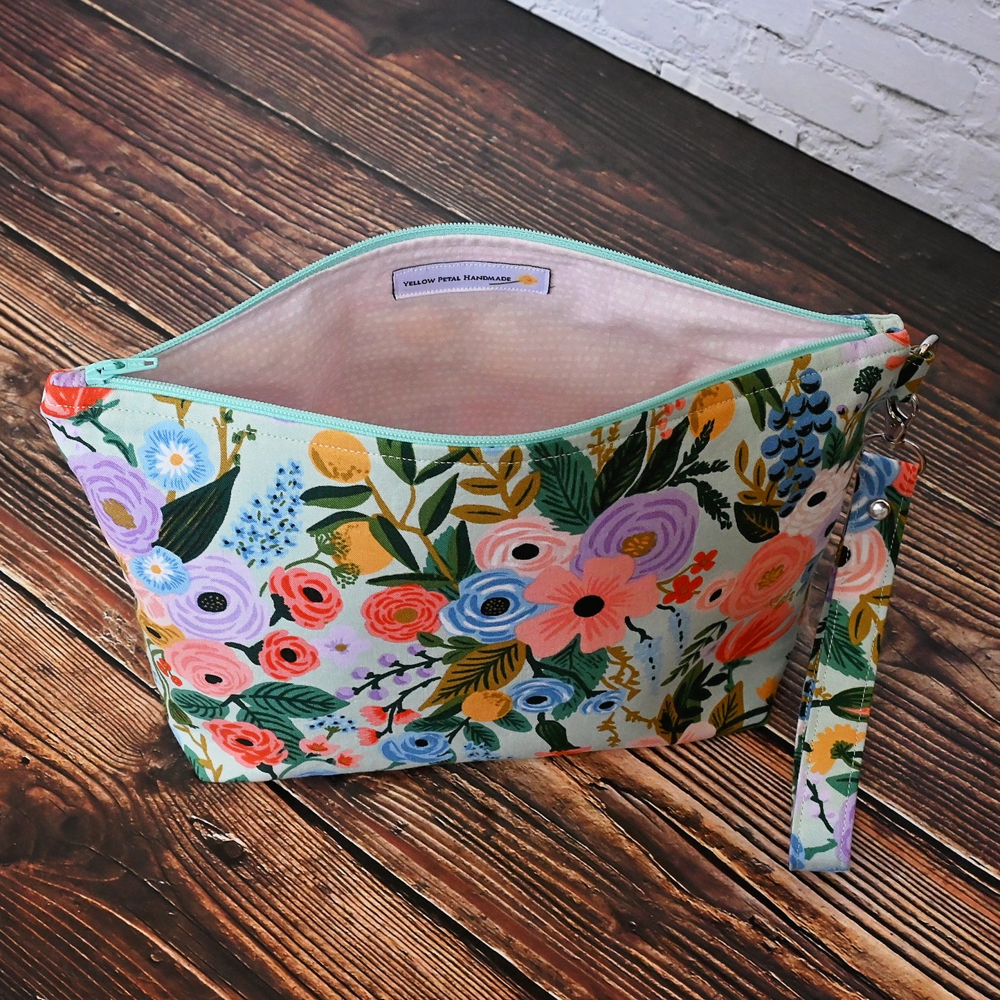 Aqua floral pouch with zipper closure and a removable wrist strap. Made from Rifle Paper Co's newest garden party collection and lined in a pale pink spotty fabric. Made in Canada by Yellow Petal Handmade.