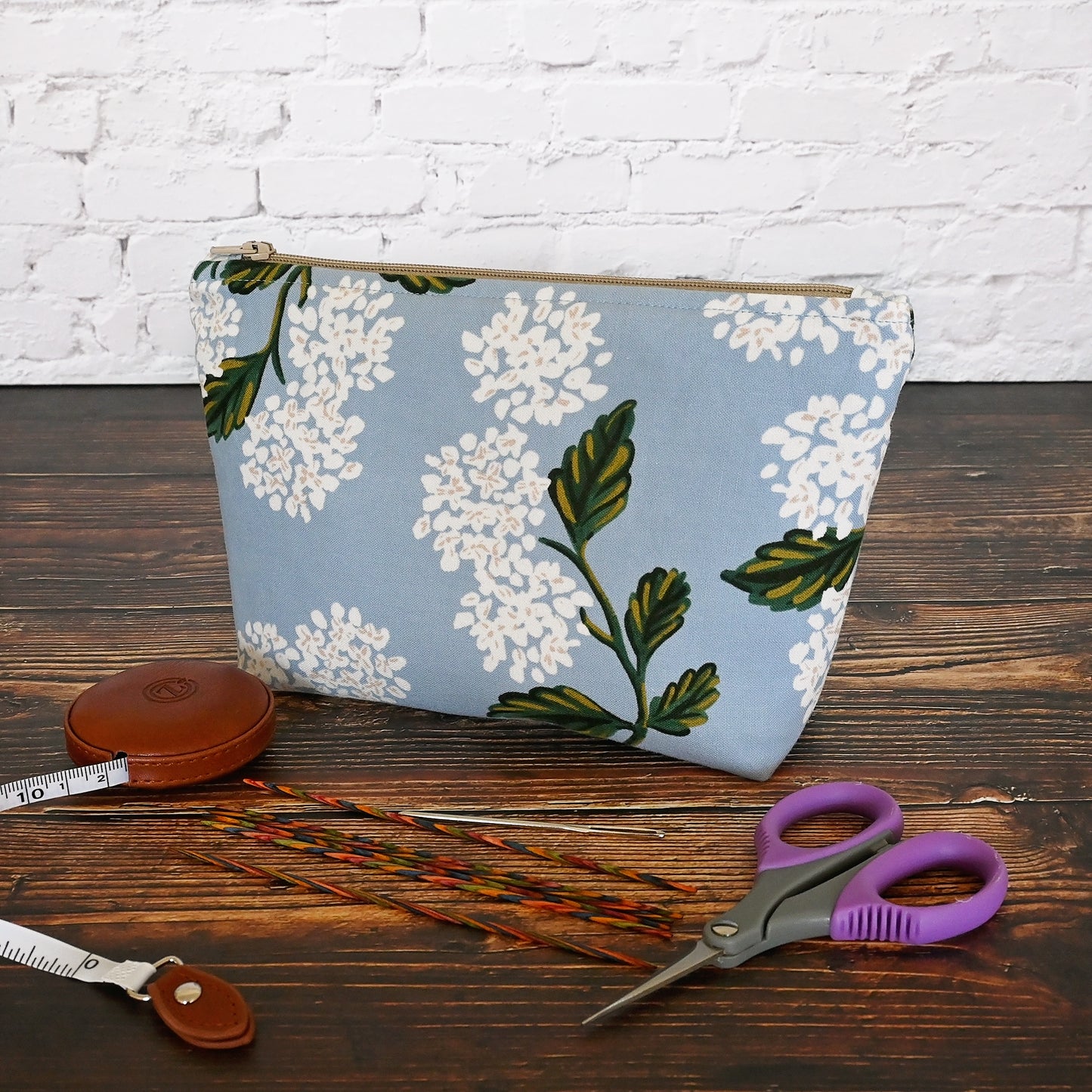 Small blue hydrangea accessory pouch made from Rifle Paper Co fabric. Zips at the top and is lined in a grey and cream striped cotton. Made in Canada by Yellow Petal Handmade.