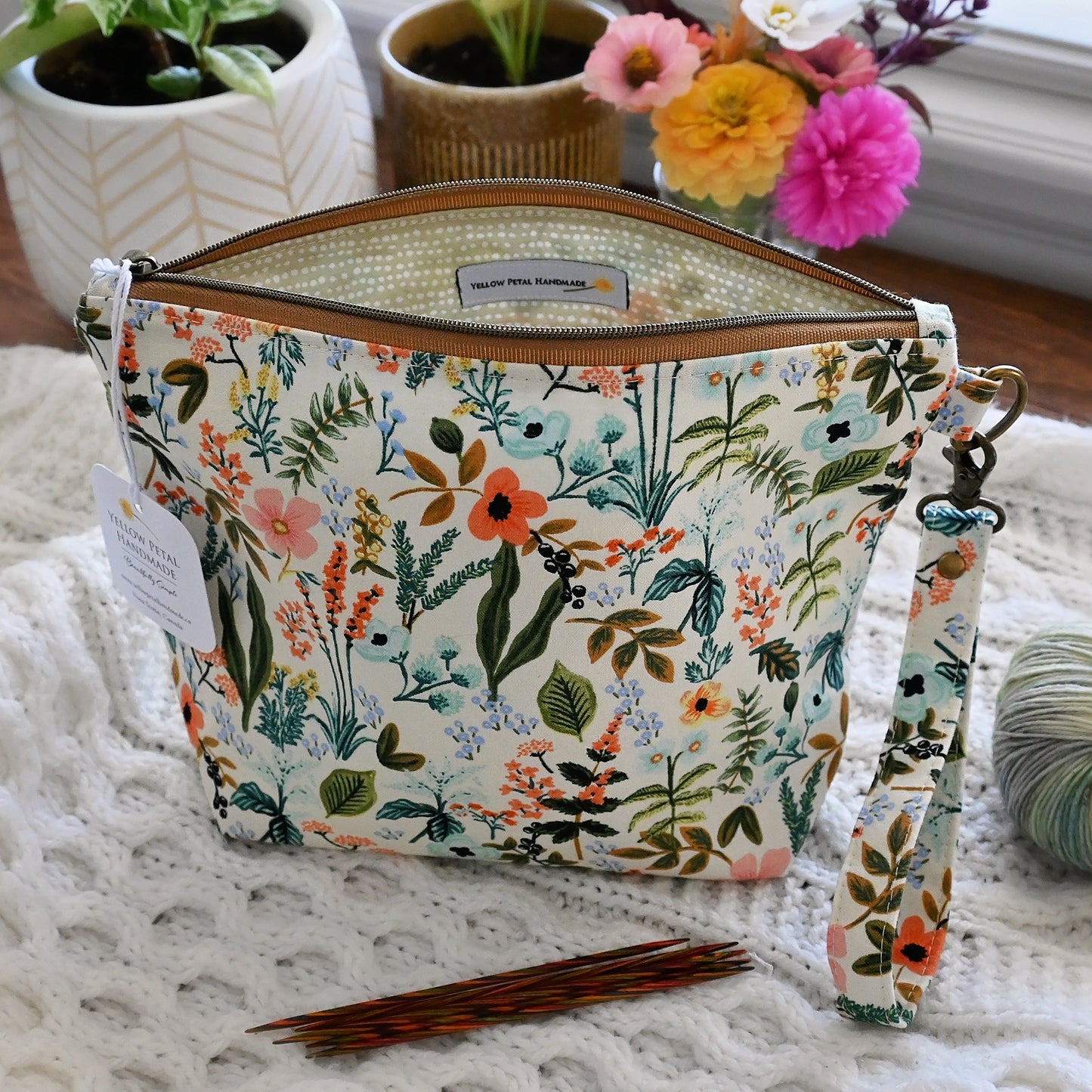 Floral-patterned project bag with a strap and zipper closure in Rifle Paper Co's Amalfi cotton, surrounded by plants and yarn.  Made in Canada by Yellow Petal Handmade.
