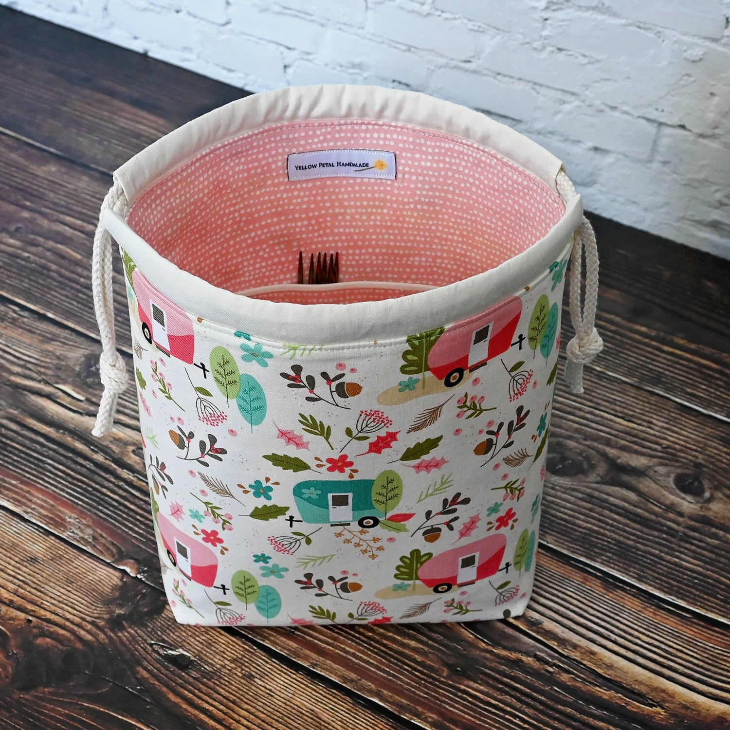 Fun camping themed project bag with pockets and a drawstring closure.  Made from the Glamp Camp collection by Riley Blake, the exterior features vintage campers along with some trees and foliage.  The interior is lined with a pretty pink and white spotty fabric from Dear Stella.  Made in Nova Scotia, Canada by Yellow Petal Handmade.