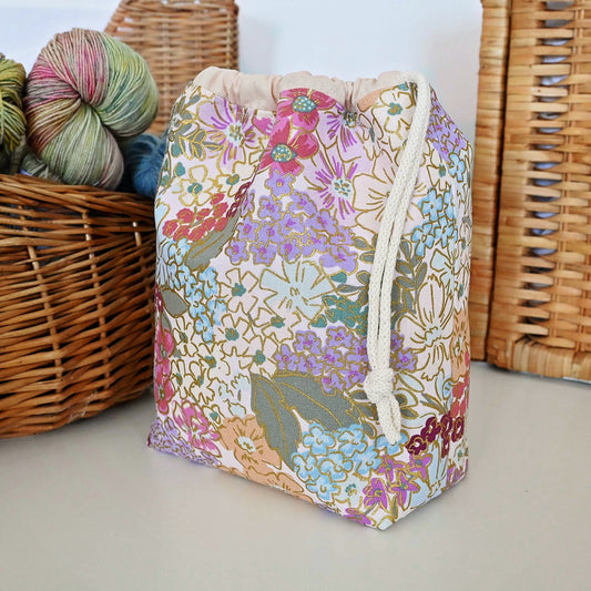 Lovely drawstring project bag in a stunning canvas.  This bag features pink, plum and blue flowers on a pretty blush background and has lovely gold metallic accents.  It has pockets for added storage and closes with a double drawstring for security.  Made in Canada by Yellow Petal Handmade.
