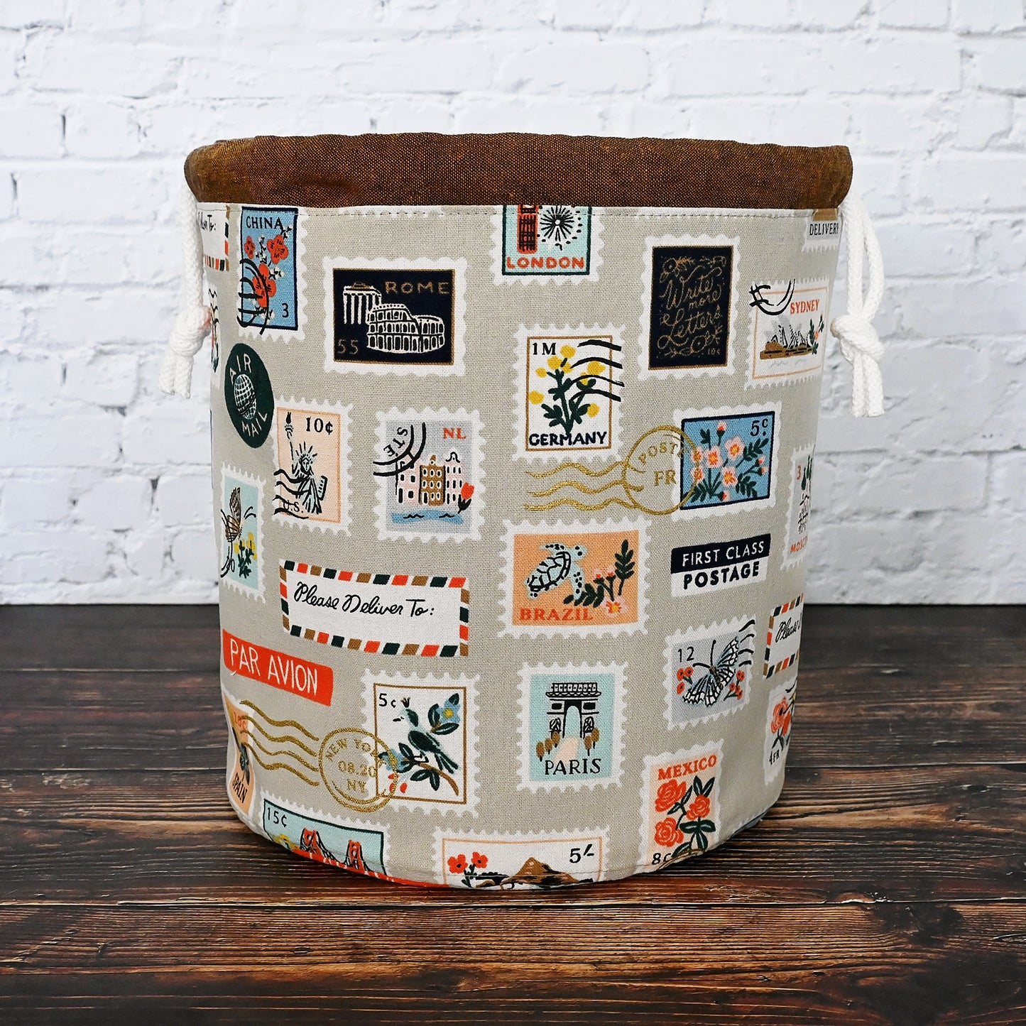 Striking canvas bucket bag is a fantastic project bag for any knitter.  Made in a fun print from the Bon Voyage collection by Rifle Paper Co, it features stamps from around the world and has metallic gold details.  It cinches closed securely with a double drawstring and brown linen casing.  Inside, you'll find multiple pockets in different sizes.  The bottom is quilted for added stability.  Made in Canada by Yellow Petal Handmade.